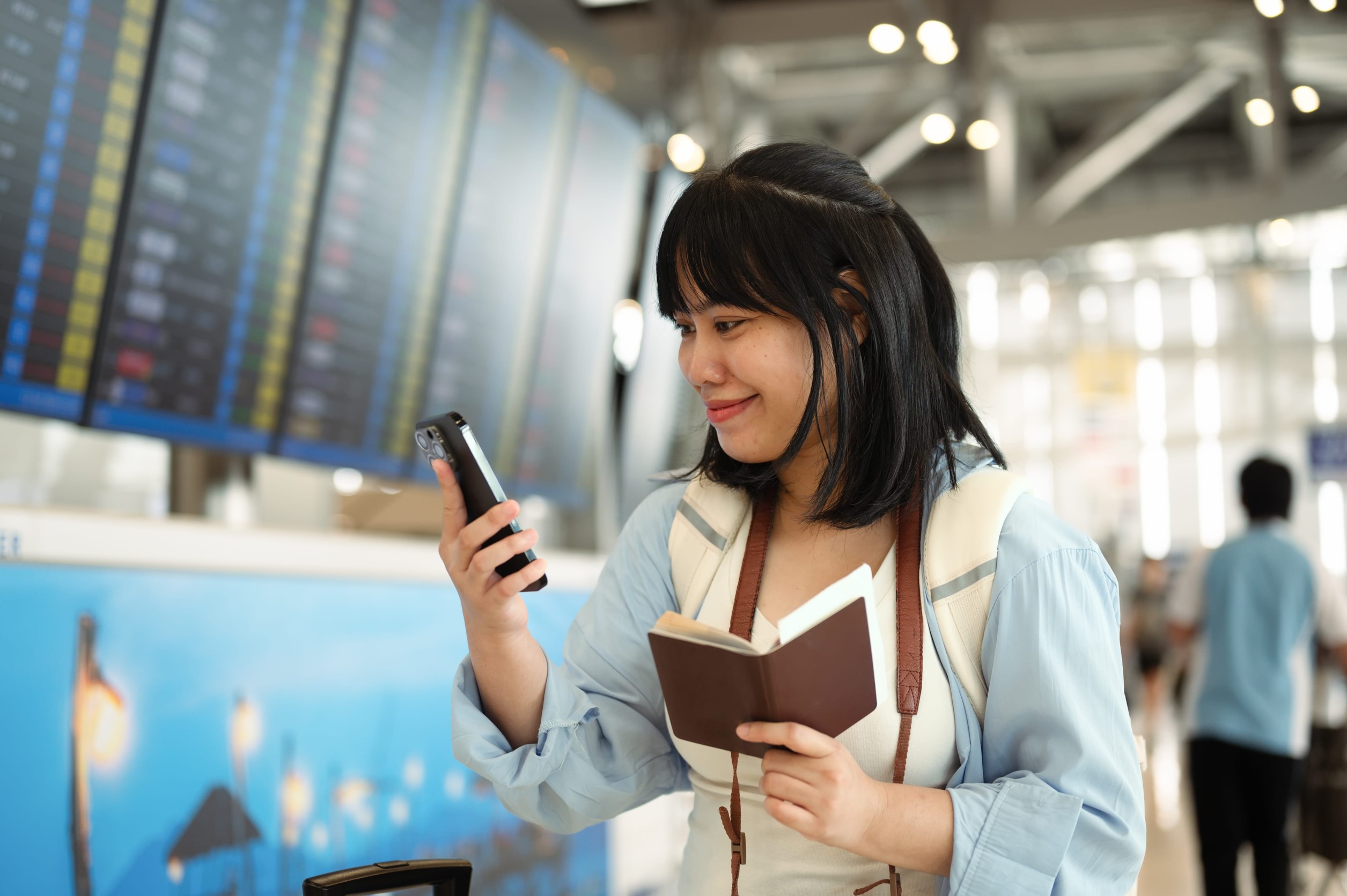 Woman holding her passport and using smartphone at an airport